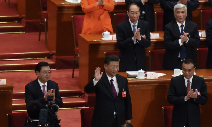 El líder del Partido Comunista Chino, Xi Jinping (centro), saluda a los asistentes con el primer ministro chino, Li Keqiang (Der.), y el miembro del Comité Permanente del Politburó del Partido Comunista de China, Li Zhanshu (Izq.), aplaudiendo a su lado, luego de ser elegido para un segundo cargo de cinco año durante la quinta sesión plenaria de la primera sesión del XIII Congreso en Beijing, China, el 17 de marzo de 2018. (Etienne Oliveau/Getty Images)