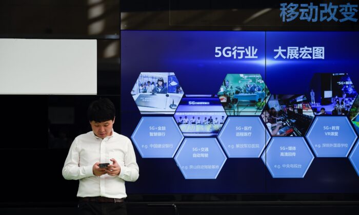 Un hombre utiliza su teléfono móvil frente a una pantalla que muestra la industria 5G de China fuera de una oficina de telecomunicaciones en Beijing el 25 de septiembre de 2019. (WANG ZHAO/AFP vía Getty Images)
