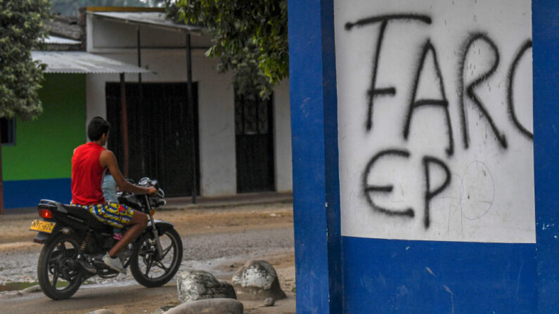 Un hombre en motocicleta pasa junto a un muro escrito que dice "FARC EP" en Arauquita, Colombia, en la frontera con Venezuela, el 23 de enero de 2022. (JUAN BARRETO/AFP vía Getty Images)