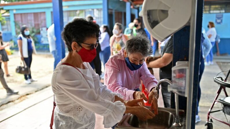 Mujeres se lavan las manos en un centro de votación durante las elecciones generales en San José, Costa Rica, el 6 de febrero de 2022. (LUIS ACOSTA/AFP vía Getty Images)