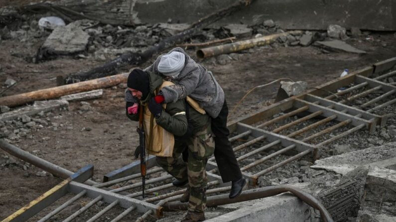 Un hombre lleva a una mujer a la espalda mientras la gente huye de la ciudad de Irpin, al oeste de Kiev, el 7 de marzo de 2022. (ARIS MESSINIS/AFP vía Getty Images)