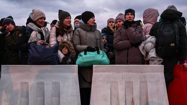 Personas que huyeron de la guerra en Ucrania esperan en la fila para subir a un autobús detrás de barreras removibles mientras oficiales de policía y soldados de la defensa territorial polaca ayudan a manejar a la multitud después de cruzar la frontera polaco-ucraniana en Medyka, Polonia, el 8 de marzo de 2022. (Omar Marques/Getty Images)