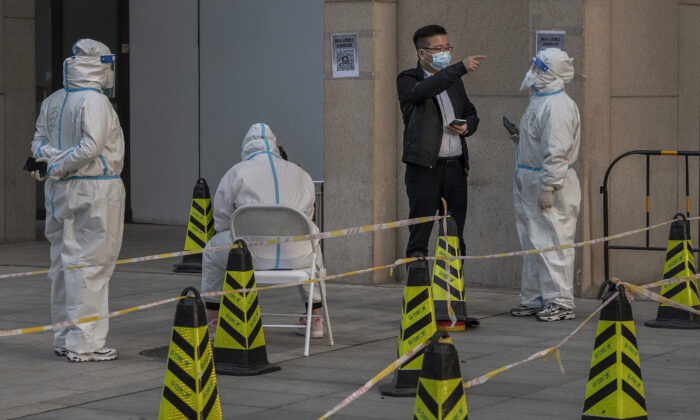 Un hombre habla con trabajadores sanitarios vestidos con ropa protectora mientras hace una pregunta en un lugar de pruebas masivas para prevenir COVID-19 en un edificio de oficinas en Beijing el 14 de marzo de 2022. (Kevin Frayer/Getty Images)