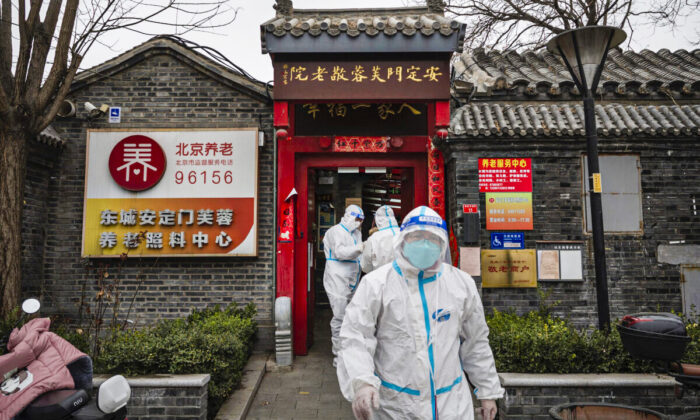 Trabajadores sanitarios llevan trajes de protección mientras permanecen en el exterior de una residencia de ancianos donde estaban realizando pruebas de ácido nucleico para detectar el COVID-19 en los residentes locales en Beijing, China, el 25 de marzo de 2022. (Kevin Frayer/Getty Images)
