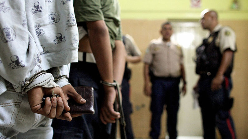 Dos adolescentes venezolanos de 15 años esposados (i) esperan mientras los policías hablan en una estación de policía luego de ser arrestados por asalto con arma mortal en el distrito de Sucre, Caracas (Venezuela) el 27 de marzo de 2009. (Thomas Coex/AFP vía Getty Images)