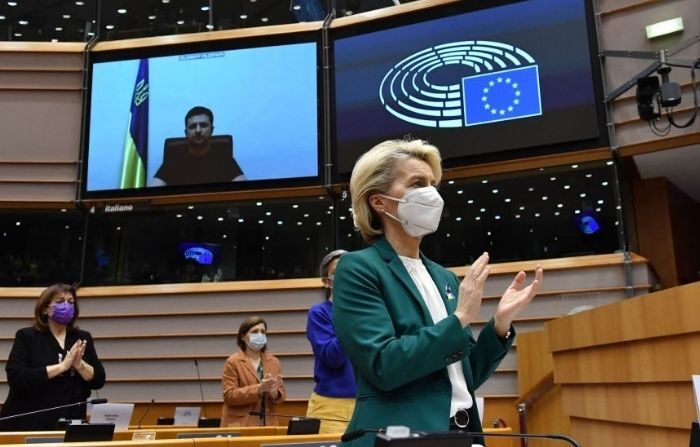 La presidenta de la Comisión Europea, Ursula von der Leyen (I), aplaude al presidente ucraniano, Volodymyr Zelensky (D), que aparece en una pantalla mientras habla en una videoconferencia durante una sesión plenaria especial del Parlamento Europeo centrada en la invasión rusa de Ucrania en la sede de la UE en Bruselas, el 1 de marzo de 2022. (JOHN THYS/AFP vía Getty Images)