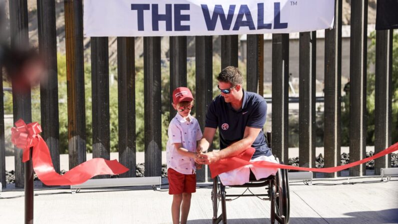 Benton Stevens, de 7 años, y Brian Kolfage, fundador de We Build the Wall, cortan la cinta en la ceremonia oficial del nuevo tramo de media milla del muro fronterizo construido con donaciones, en Sunland Park, N.M., el 30 de mayo de 2019. (Charlotte Cuthbertson/The Epoch Times)
