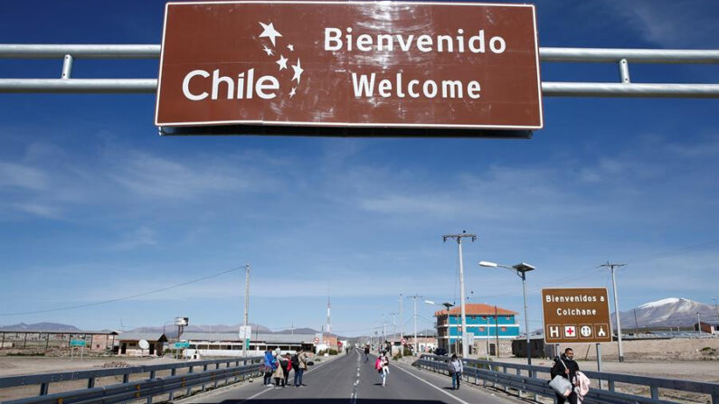 Migrantes caminan bajo un cartel que señala la entrada a Chile, el 13 de febrero de 2022, en los alrededores de la fronteriza comuna de Colchane (Chile), en una fotografía de archivo. EFE/ José Caviedes