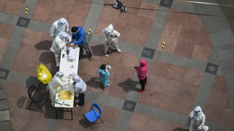 Un trabajador sanitario con equipo de protección personal (abajo a la izquierda) toma un hisopo para las pruebas de COVID-19 en un recinto durante un cierre en el distrito de Jing'an en Shanghái el 10 de abril de 2022. (Hector Retamal/AFP vía Getty Images)
