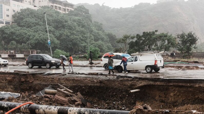 Unas personas pasan por el asentamiento informal de Quarry road, en las afueras de Durban (Sudáfrica), el 18 de abril de 2022, mientras empieza a llover de nuevo después de que los vientos, las fuertes lluvias y los desprendimientos de tierra destruyeran muchas casas e infraestructuras la semana pasada. (Rajesh Jantilal/AFP vía Getty Images)