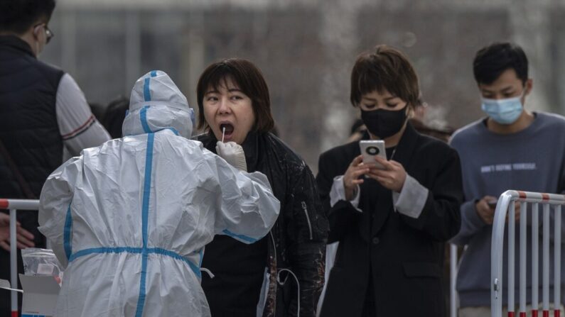 Una trabajadora médica lleva ropa de protección mientras realiza una prueba de ácido nucleico a una mujer en un centro de pruebas masivas para prevenir la propagación del COVID-19 en Beijing, China, el 15 de marzo de 2022. (Kevin Frayer/Getty Images)
