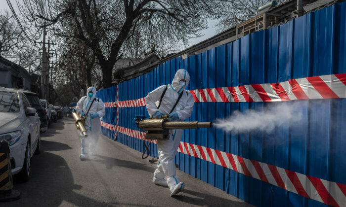 Trabajadores sanitarios llevan trajes de protección mientras desinfectan una zona fuera de una comunidad confinada por el control sanitario después de que se encontraran casos recientes de COVID-19, en Beijing, China, el 28 de marzo de 2022. (Kevin Frayer/Getty Images)