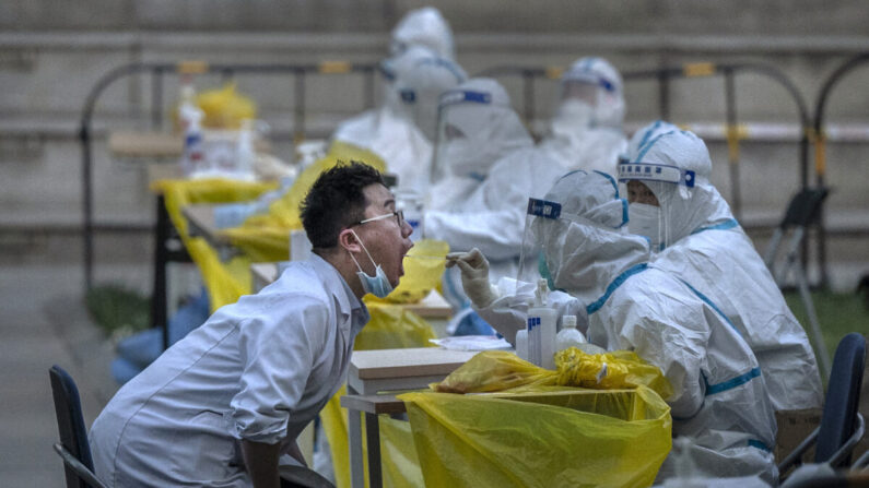 Un trabajador sanitario lleva un traje de protección mientras toma un hisopado de un empleado de una empresa local para obtener una muestra para las pruebas de ácido nucleico para el virus COVID-19 en un sitio de pruebas improvisado en el distrito de Haidian el 26 de abril de 2022 en Beijing, China. (Kevin Frayer/Getty Images)