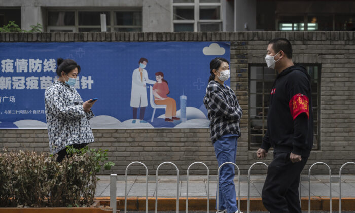 La gente espera en la fila para las pruebas de ácido nucleico para detectar COVID-19 junto a un cartel de vacunas en un sitio de prueba improvisado en el Distrito Comercial Central en Chaoyang en Beijing, China, el 27 de abril de 2022. (Kevin Frayer/Getty Images)