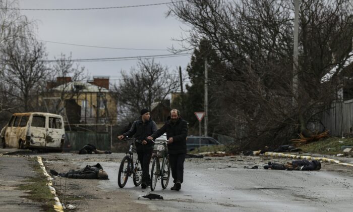 Dos personas empujan su bicicleta mientras cruzan una calle en Bucha, al noroeste de Kiev, Ucrania, el 2 de abril de 2022. (Ronaldo Schemidt/AFP vía Getty Images)
