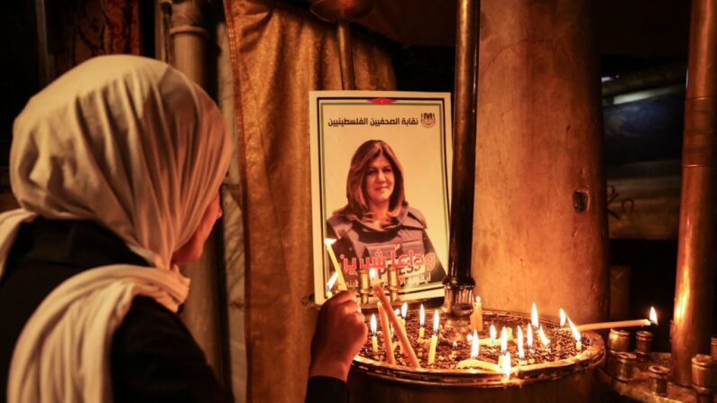 Una mujer enciende una vela frente a un póster que representa a la veterana periodista de Al-Jazeera Shireen Abu Akleh en la Iglesia de la Natividad en la ciudad bíblica de Belén, en Cisjordania, el 11 de mayo de 2022. (Hazem Bader/AFP vía Getty Images)