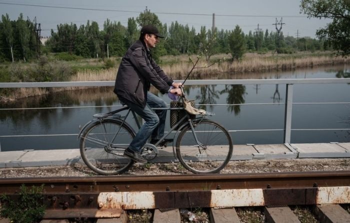 Un hombre conduce una bicicleta en un puente ferroviario sobre un río en Slovyansk, en el este de Ucrania, el 8 de mayo de 2022, en medio de la invasión rusa de Ucrania. (YASUYOSHI CHIBA/AFP vía Getty Images)