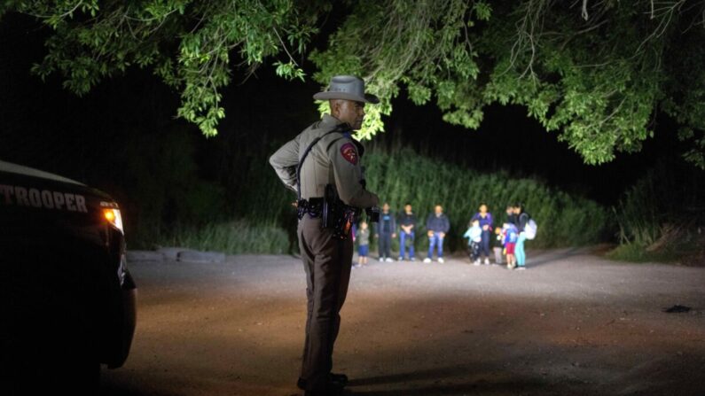 Un policía estatal de Texas vigila a los extranjeros ilegales mientras esperan ser detenidos por los agentes de la Patrulla Fronteriza de Estados Unidos en Del Río, Texas, el 19 de mayo de 2021. (John Moore/Getty Images)
