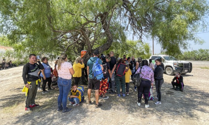 Un numeroso grupo de inmigrantes ilegales se agrupa bajo la sombra de un árbol mientras los agentes de la Patrulla Fronteriza organizan el transporte cerca de Eagle Pass, Texas, el 20 de mayo de 2022. (Charlotte Cuthbertson/The Epoch Times)