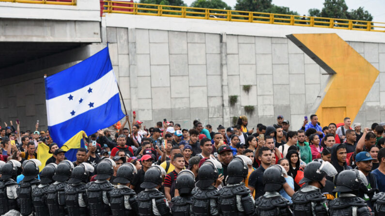 Miembros de la Guardia Nacional hacen guardia mientras migrantes de Centro y Sudamérica con una bandera de Honduras participan en una caravana hacia la frontera con Estados Unidos, en Tapachula, estado de Chiapas, México, el 6 de junio de 2022. (ISAAC GUZMAN/AFP vía Getty Images)