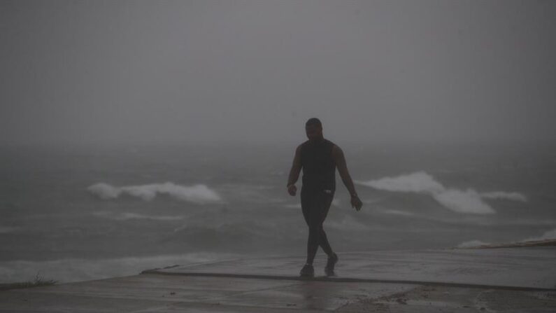 Un hombre camina bajo una intensa lluvia en un malecón, en una fotografía de archivo. EFE/Orlando Barría
