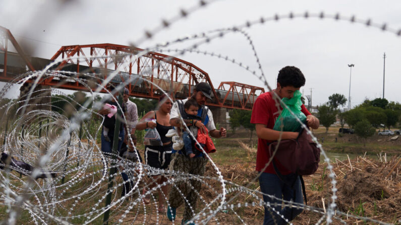 Migrantes que cruzaron ilegalmente el Río Grande caminan junto a las concertinas en Eagle Pass, Texas, el 22 de mayo de 2022. (Allison Dinner/AFP vía Getty Images)
