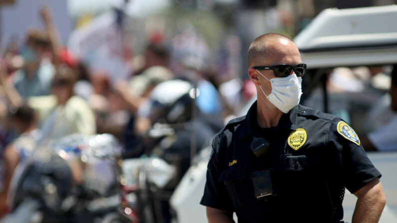 Un oficial del Departamento de Policía de San Diego mira mientras los manifestantes sostienen pancartas y corean contra las medidas del gobierno estatal por el COVID-19 durante una manifestación de Open California el 26 de abril de 2020 en San Diego, California. (Sean M. Haffey/Getty Images)

