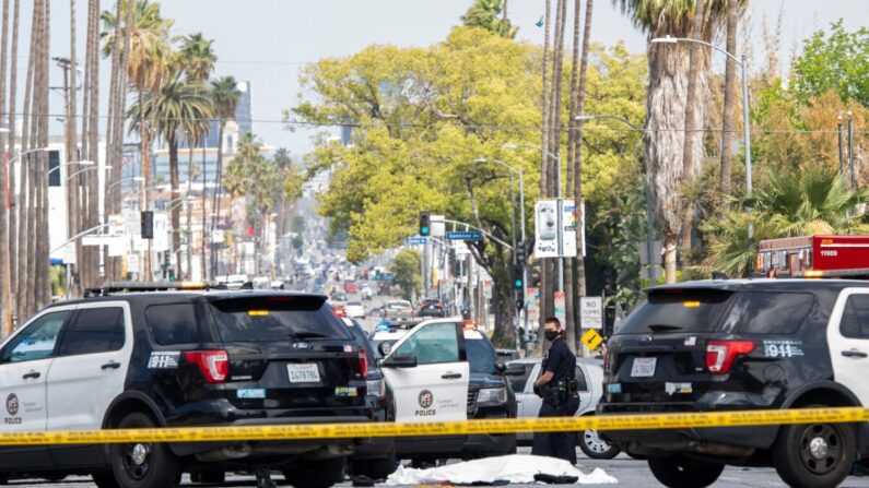 En una fotografía de archivo, agentes del Departamento de Policía de Los Ángeles permanecen en la esquina de Fairfax Avenue y Sunset Boulevard, donde un cuerpo cubierto con una sábana blanca yace en el pavimento, en Los Ángeles, el 24 de abril de 2021. (Valerie Macon/AFP vía Getty Images)
