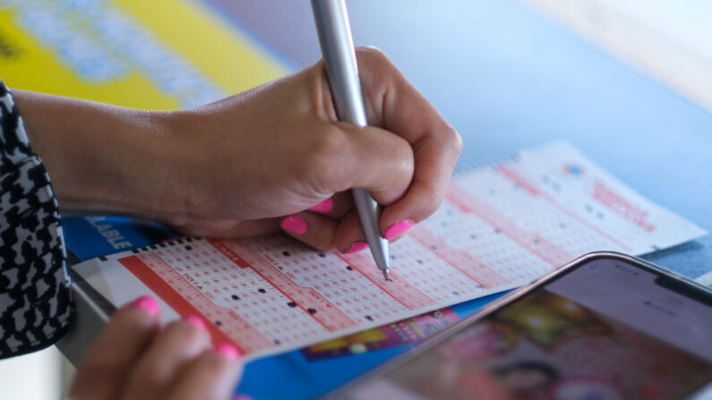 Una mujer comprueba los números elegidos para sus boletos de la lotería Mega Millions en una tienda de conveniencia 7-Eleven en Chino Hills, California, el 28 de julio de 2022. (Ringo Chiu/AFP vía Getty Images)