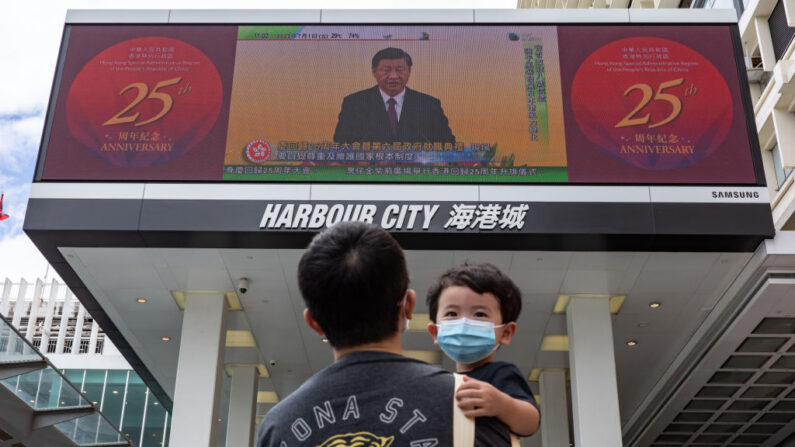 Un hombre con un niño en brazos camina frente a una pantalla que muestra una transmisión en vivo del presidente chino Xi Jinping hablando durante una ceremonia de juramento del nuevo jefe ejecutivo de Hong Kong, John Lee, el 01 de julio de 2022 en Hong Kong, China. (Anthony Kwan/Getty Images)