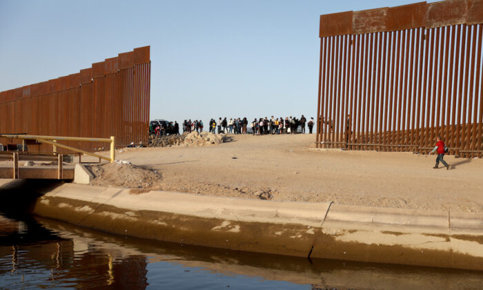 Inmigrantes ilegales cerca de una brecha en la barrera fronteriza entre Estados Unidos y México, esperan para ser procesados por la Patrulla Fronteriza de Estados Unidos en Yuma, Arizona, el 20 de mayo de 2022. (Mario Tama/Getty Images)