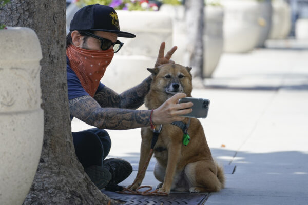 Andrew Stuart lleva un pañuelo como máscara mientras se toma un selfie con su perro, Voltron, en Sunset Blvd, en West Hollywood, California, el 2 de julio del 2020. (Ashley Landis/AP Photo)