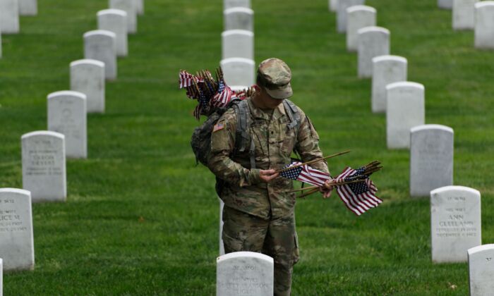 Un miembro del Ejército de EE.UU. coloca banderas estadounidenses en una tumba, en el Cementerio Nacional de Arlington, el 25 de mayo de 2017. (Brendan Smialowski/AFP vía Getty Images)
