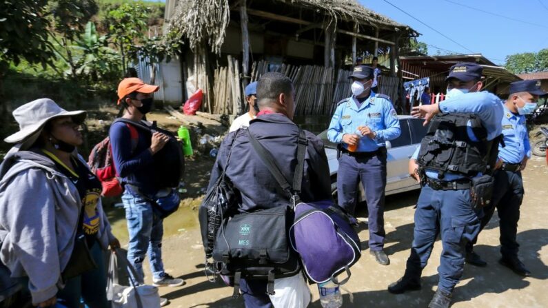 Migrantes que quieren llegar a Estados Unidos, en su mayoría hondureños y nicaragüenses, hablan con policías a su llegada a la frontera entre Honduras y Guatemala, en Corinto, Honduras, el 15 de enero de 2022. (WENDELL ESCOTO/AFP vía Getty Images)