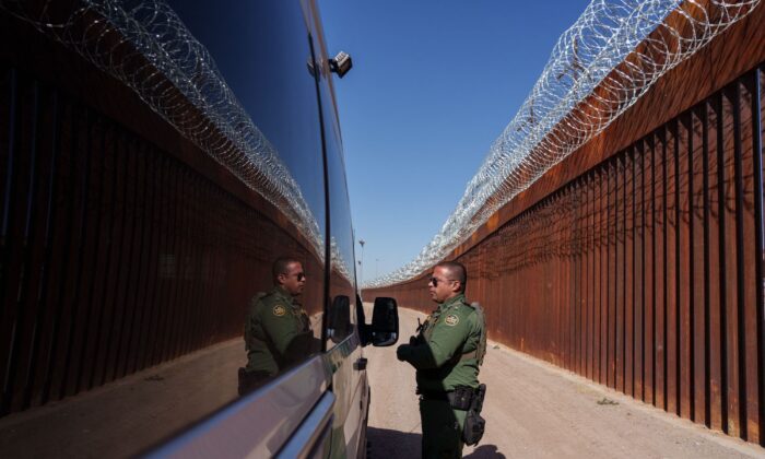 El agente de la Patrulla Fronteriza de Estados Unidos, Carlos Rivera, se ve reflejado en los laterales de un vehículo mientras habla con otro agente a lo largo del muro fronterizo, en el centro de El Paso, Texas, el 3 de junio de 2022. (Paul Ratje/AFP vía Getty Images)