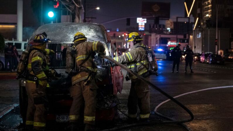 Bomberos laboran en la escena sobre un vehículo de transporte colectivo quemado luego de que fuera incendiado por individuos no identificados en Tijuana, estado de Baja California, México, el 12 de agosto de 2022.  (Foto de GUILLERMO ARIAS/AFP a través de Getty Images)
