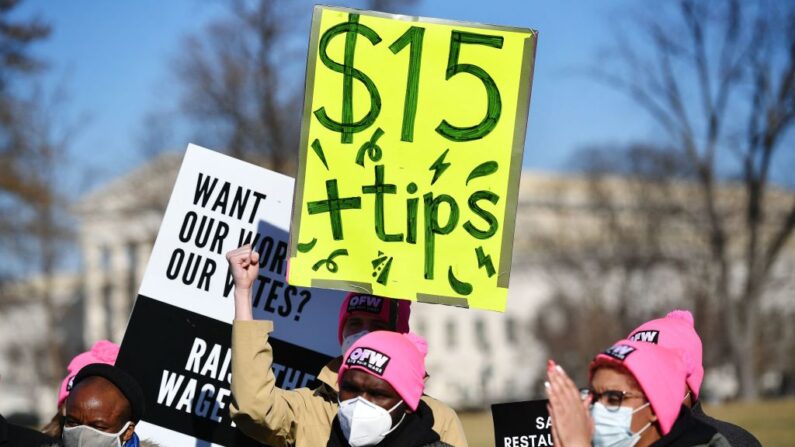 Activista sostiene una pancarta exigiendo un salario mínimo de 15 dólares/hora y propinas para los trabajadores de los restaurantes durante una manifestación para pedir una ayuda adicional en el Triángulo de la Cámara del Capitolio de Estados Unidos en Washington, DC, el 8 de febrero de 2022. (Mandel Ngan/AFP vía Getty Images)