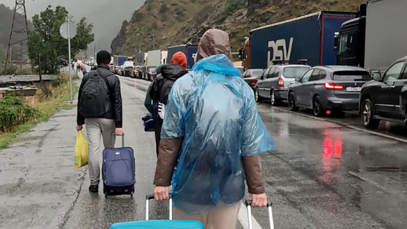 Personas con equipaje pasan junto a vehículos con matrículas rusas en el lado ruso de la frontera hacia el puesto de control aduanero de Nizhniy Lars, entre Georgia y Rusia, a unos 25 km de la ciudad de Vladikavkaz, el 25 de septiembre de 2022. (AFP vía Getty Images)