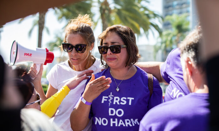 Abigail Martinez (der.), la madre de una adolescente transgénero que se suicidó, derrama lágrimas mientras Erin Friday la consuela y los activistas transgénero bloquean las cámaras de televisión para que no graben su historia, en Anaheim, California, el 8 de octubre de 2022. (John Fredricks/The Epoch Times)
