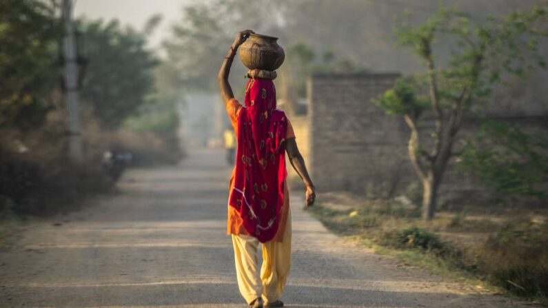Una mujer india camina mientras sostiene una olla de tierra en su cabeza después de llenarla de una toma de agua común en la aldea de Mohatabad en las afueras de Faridabad en el estado norteño indio de Haryana el 4 de abril de 2019. (Money Sharma/AFP vía Getty Images)