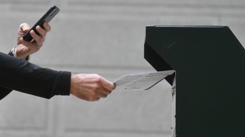 Un hombre se fotografía depositando su papeleta en una urna oficial mientras una larga fila de votantes hace fila fuera del Ayuntamiento de Filadelfia en el colegio electoral satélite en Filadelfia, Pensilvania, el 27 de octubre de 2020. (Mark Makela/Getty Images)
