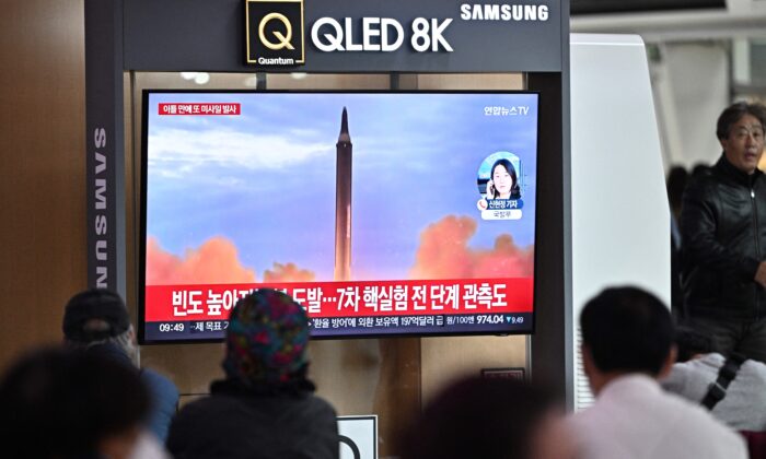 Personas sentadas cerca de un televisor que muestra un noticiero con imágenes de archivo de una prueba de misiles norcoreanos, en una estación de tren en Seúl el 6 de octubre de 2022. (Anthony Wallace/AFP vía Getty Images)