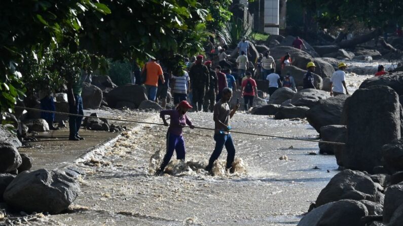 Los residentes utilizan una cuerda para cruzar una calle en medio de rocas y agua que corren por una calle en El Castaño, un barrio de Maracay, la capital del estado de Aragua, al norte de Venezuela, el 18 de octubre de 2022. (Federico Parra/AFP vía Getty Images)