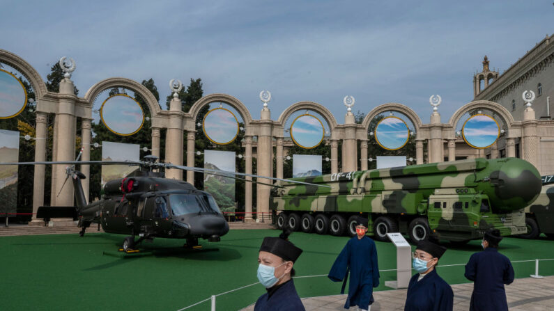Miembros del Partido visten túnicas religiosas tradicionales mientras observan un helicóptero y un lanzamisiles como parte de una exhibición de material militar en una exposición que destaca los años del presidente Xi Jinping como líder, como parte del próximo 20º Congreso del Partido, el 12 de octubre de 2022 en Beijing, China. (Kevin Frayer/Getty Images)
