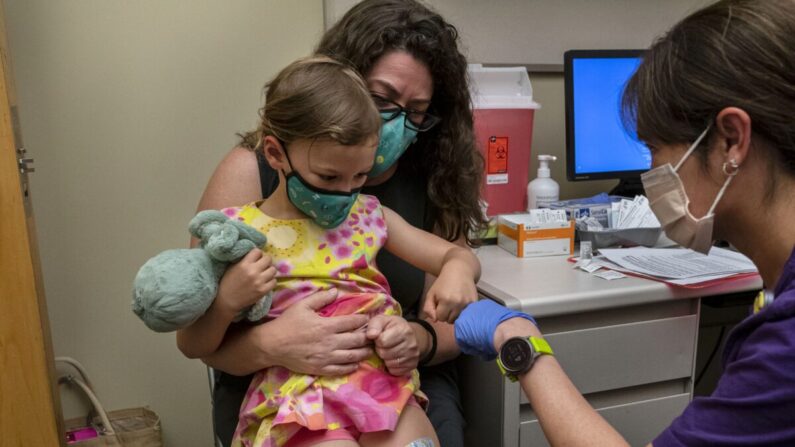 Nora Burlingame, de 3 años, se sienta en el regazo de su madre, Dina Burlingame, y recibe un choque de puños de la enfermera Luann Majeed después de recibir su primera dosis de la vacuna anti-COVID de Pfizer en el Centro Médico UW-Roosevelt, en Seattle, Washington, el 21 de junio de 2022. (David Ryder/Getty Images)