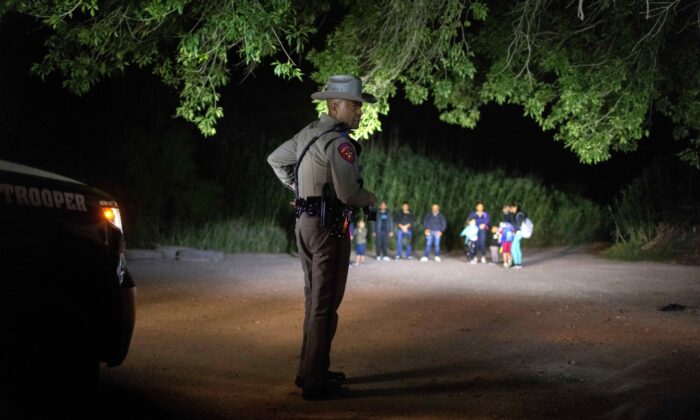 Un policía estatal de Texas vigila a los extranjeros ilegales mientras esperan ser detenidos por los agentes de la Patrulla Fronteriza de Estados Unidos en Del Río, Texas, el 19 de mayo de 2021. (John Moore/Getty Images)