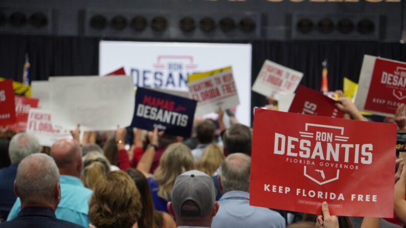 El gobernador de Florida, Ron DeSantis, sube al escenario en un gimnasio universitario repleto en el condado rural de Columbia el 3 de noviembre de 2022, mientras los asistentes se ponen de pie, vitoreando y agitando carteles de campaña. (Nanette Holt/The Epoch Times)