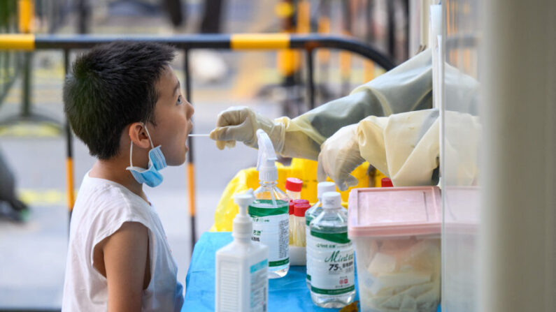 Un empleado de la salud está tomando una muestra de hisopo de un niño para hacerle la prueba de COVID-19 en Guangzhou, en la provincia de Guangdong, en el sur de China, el 31 de julio de 2022. (STR/AFP a través de Getty Images)
