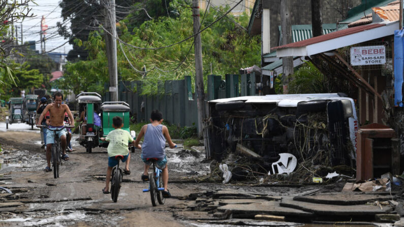 Los residentes pasan en bicicleta junto a un vehículo volcado en un pueblo afectado por las inundaciones en la ciudad de Noveleta, provincia de Cavite (Filipinas), el 31 de octubre de 2022, días después del paso de la tormenta tropical Nalgae. (Ted Aljibe/AFP vía Getty Images)