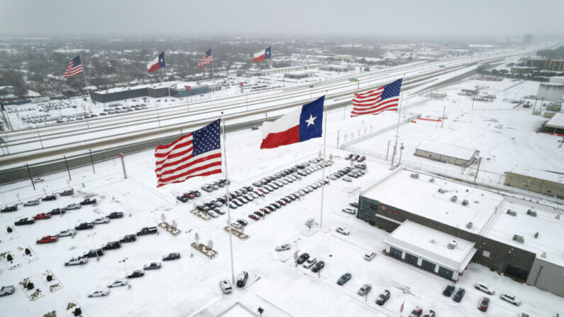 En una vista aérea, las banderas de Estados Unidos y del estado de Texas ondean sobre los concesionarios de automóviles mientras el tráfico ligero se mueve a través de la nieve y el hielo en la Ruta 183 de Estados Unidos el 03 de febrero de 2022 en Irving, Texas. (John Moore/Getty Images)